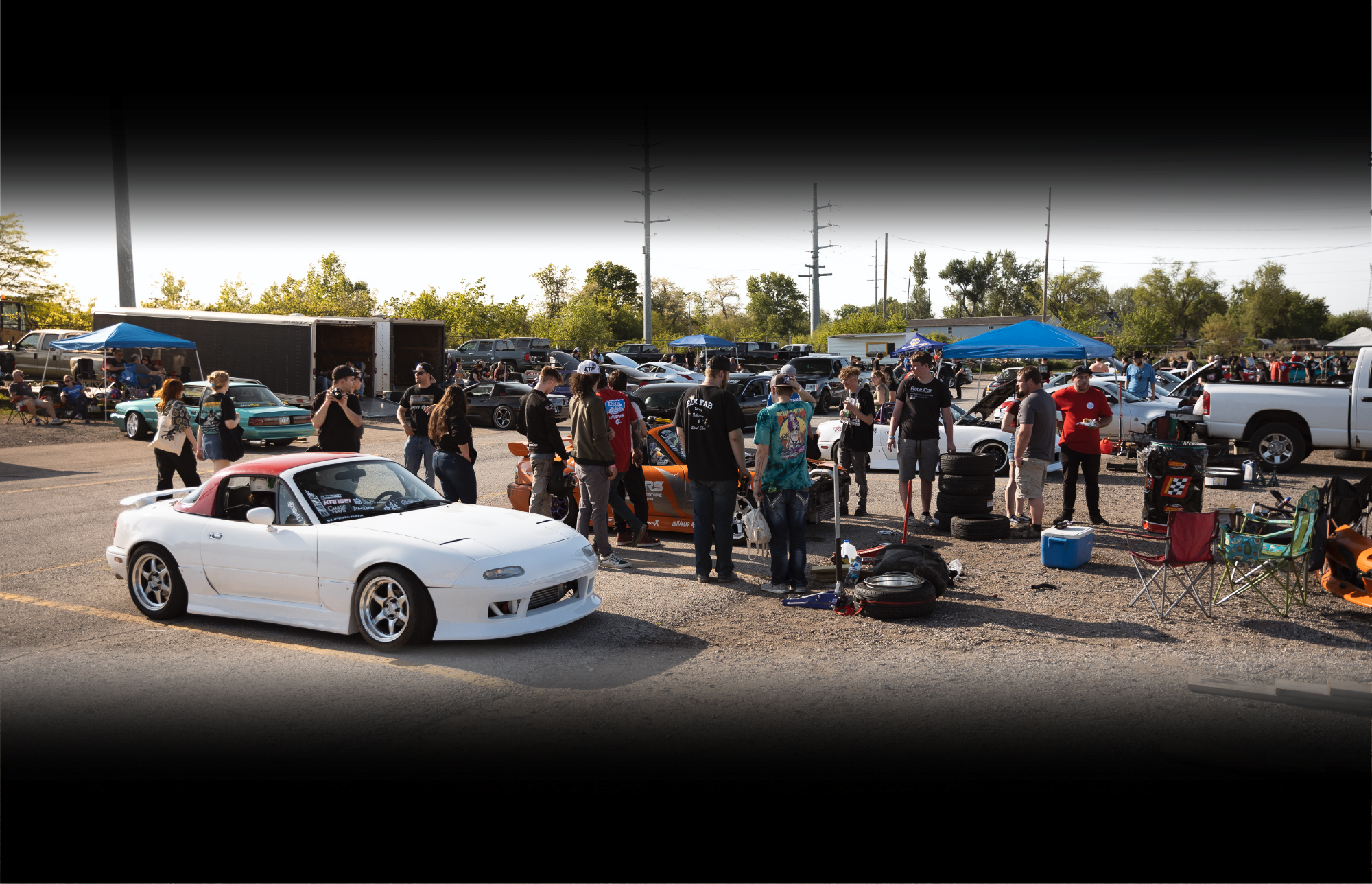 white miata drift car in the foreground of a parking lot with spectators walking around. cars in the background.